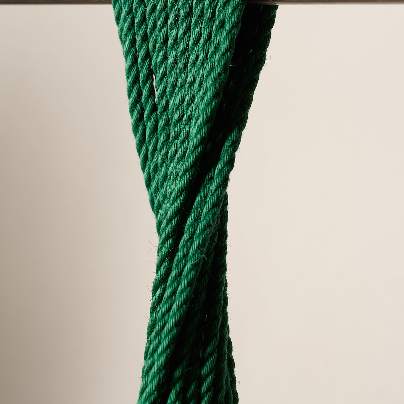 A close-up of a 6mm, jute, dark green twisted rope or cord draped over a horizontal metal rod against a plain light beige background.