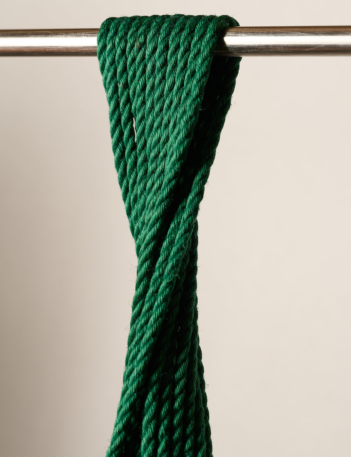 A close-up of a 6mm, jute, dark green twisted rope or cord draped over a horizontal metal rod against a plain light beige background.