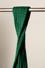 A close-up of a 6mm, jute, dark green twisted rope or cord draped over a horizontal metal rod against a plain light beige background.