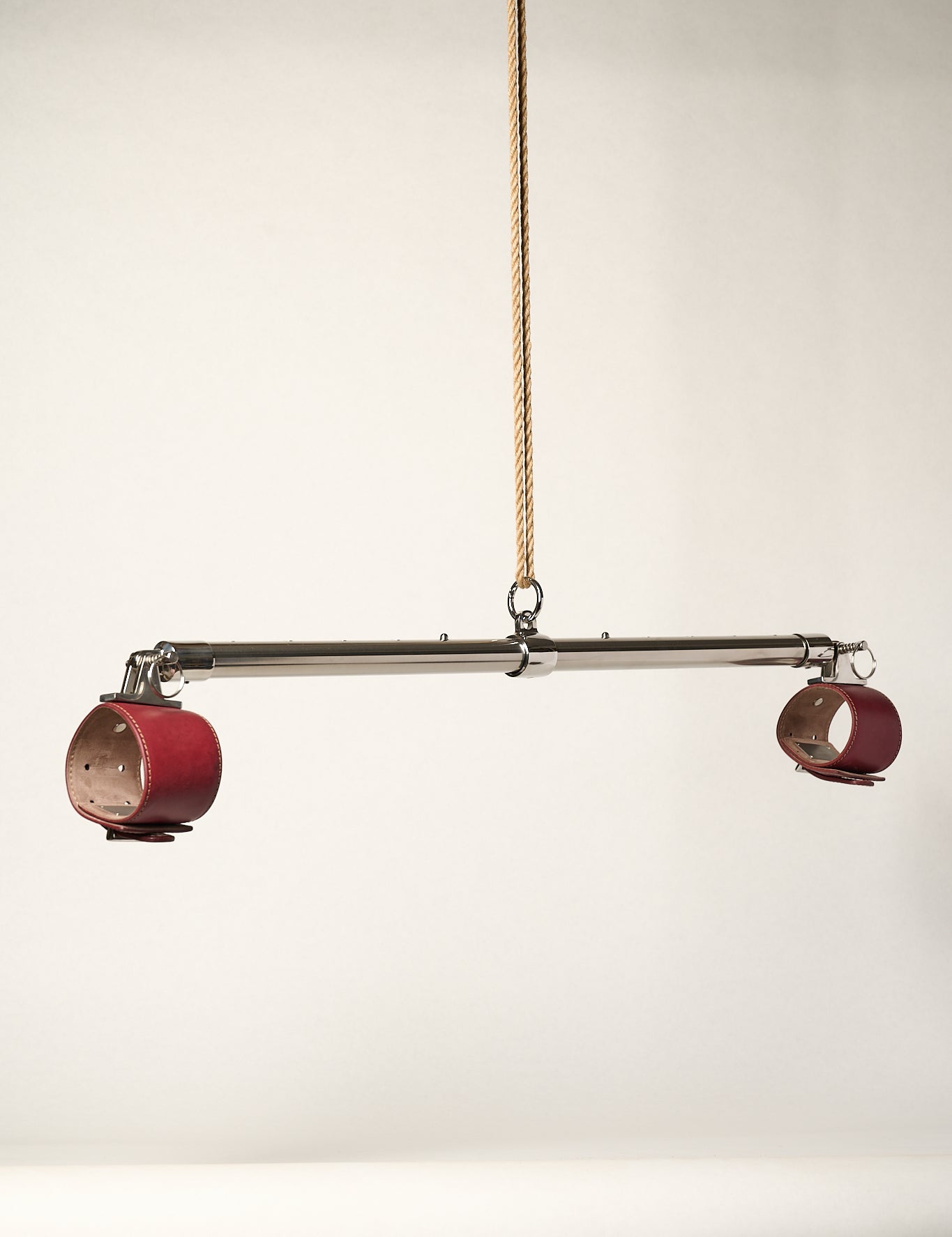 burgundy cuffs attached to silver metal bar hanging from rope