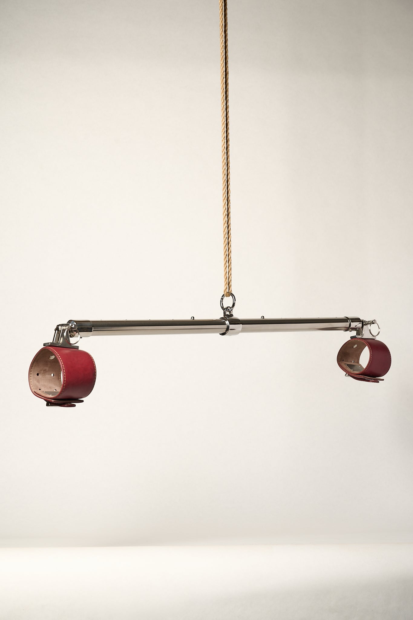 burgundy cuffs attached to silver metal bar hanging from rope