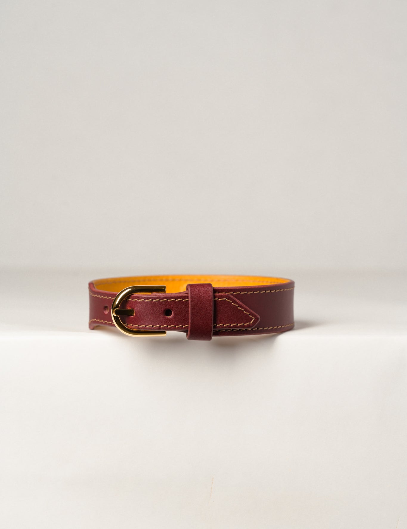 A close-up image of a luxury leather necklace with a gold stainless steel buckle, predominantly burgundy in color.