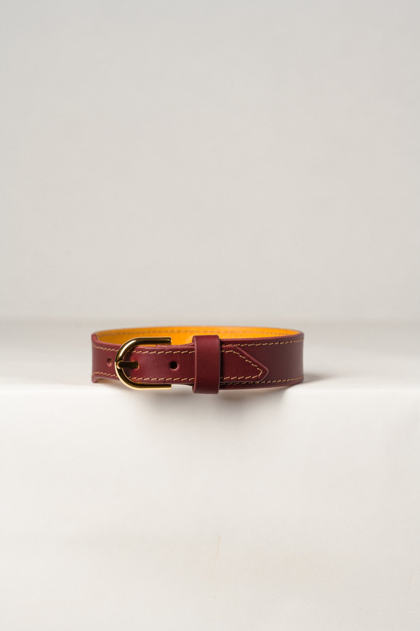 A close-up image of a luxury leather necklace with a gold stainless steel buckle, predominantly burgundy in color.
