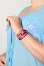 A close-up of a person wearing a pink leather triple-strand bracelet with a silver buckle, paired with a light blue floral printed top.