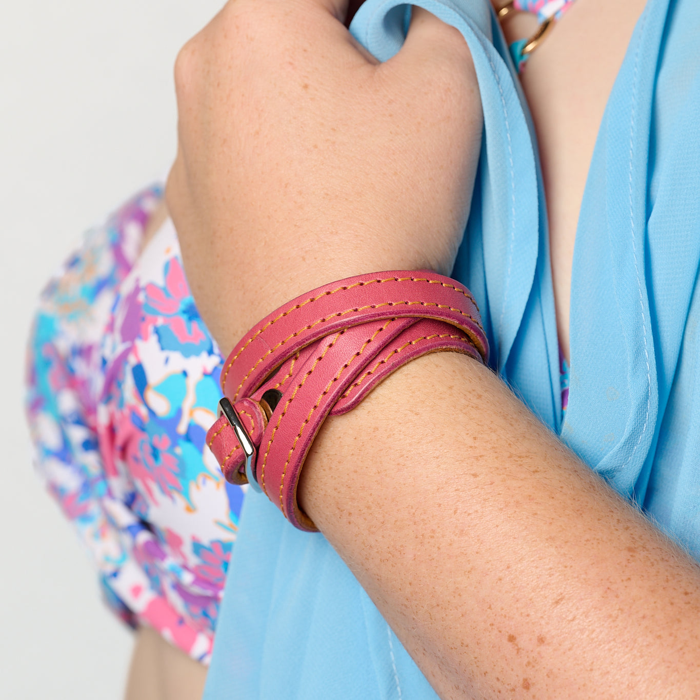 A close-up of a person wearing a pink wrap-style leather bracelet, holding a light blue top. A colorful floral-patterned top is also visible.