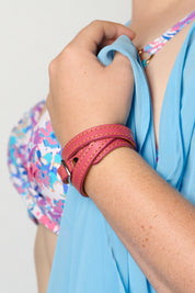 A close-up of a person wearing a pink wrap-style leather bracelet, holding a light blue top. A colorful floral-patterned top is also visible.