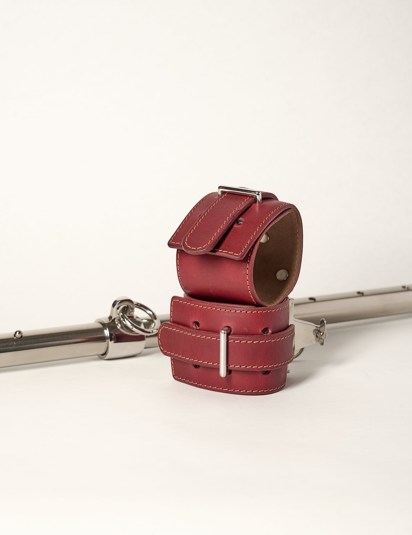 burgundy cuffs sitting in front of adjustable silver metal bar with o-ring