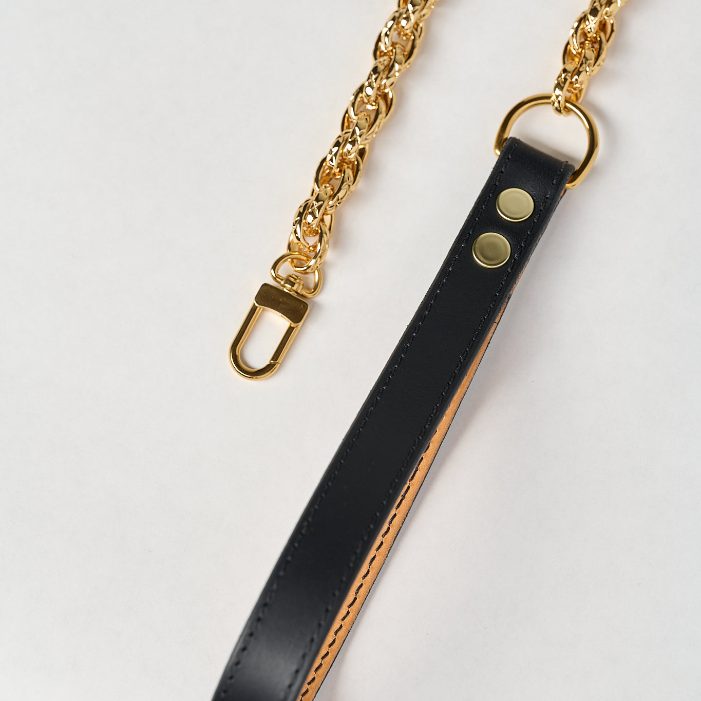 Black leather strap with gold chain on a white background