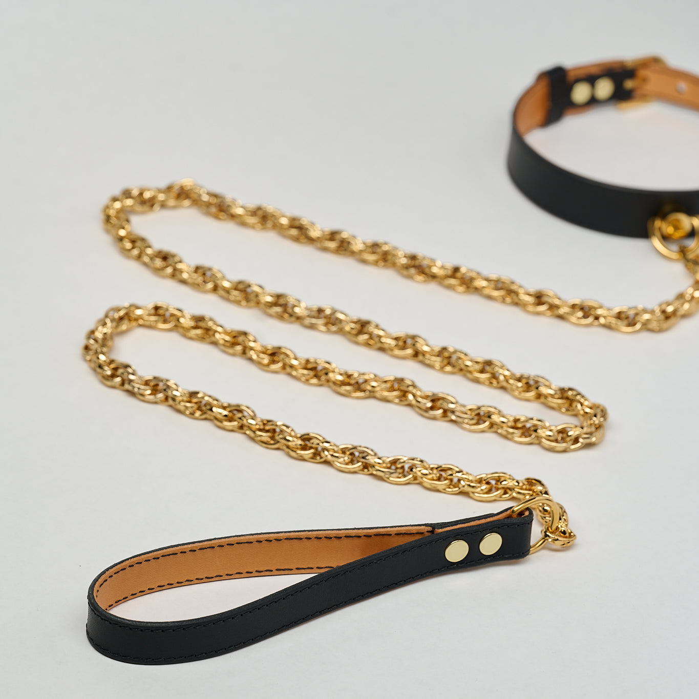 Black leather strap attached to black leather necklace choker with gold chain on a light gray background