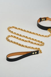 Black leather strap attached to black leather necklace choker with gold chain on a light gray background