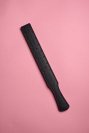 A black leather strap with a fenestrated surface, laid on a pink background.