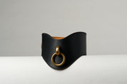 Black leather necklace with a gold ring on a light gray background