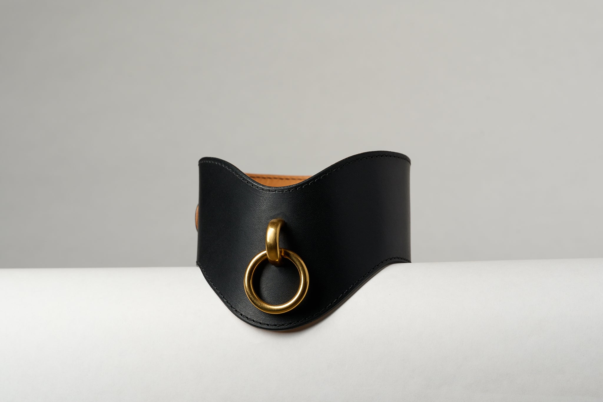 Black leather necklace with a gold ring on a light gray background