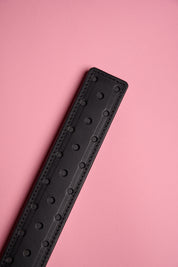 A black leather strap with a fenestrated surface, laid on a pink background.