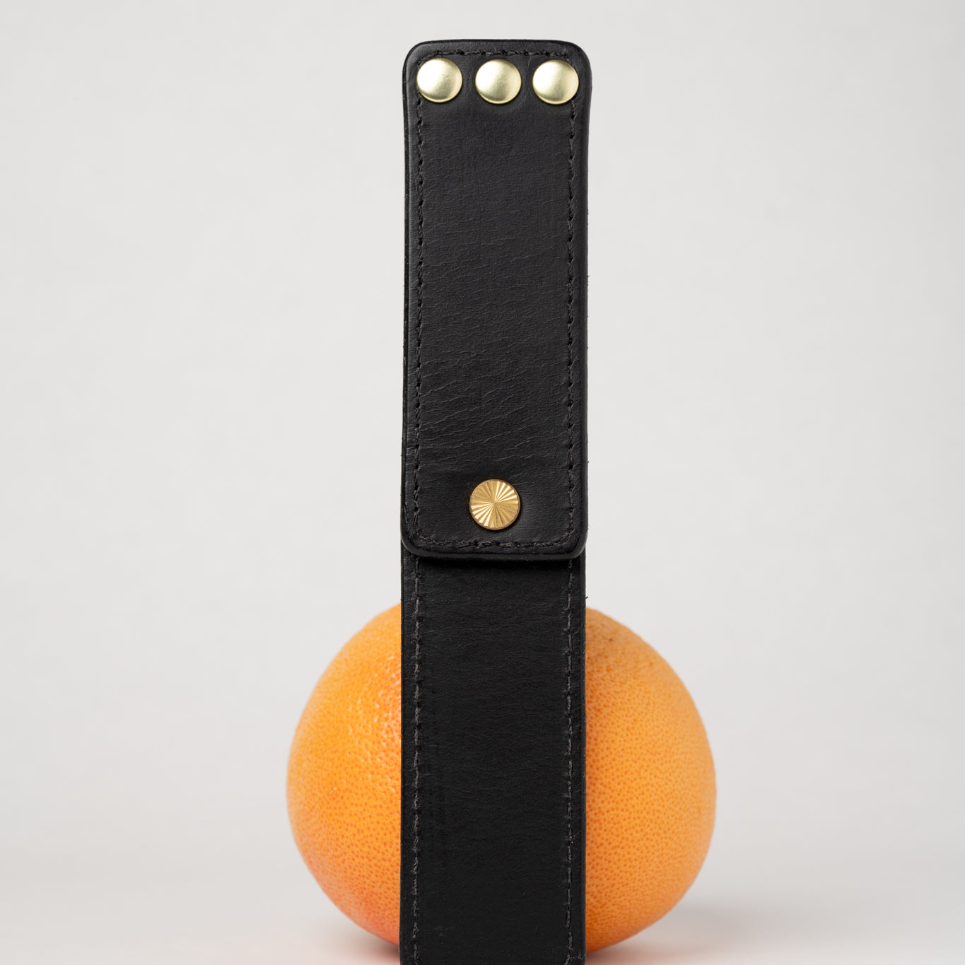 foldable black  leather travel size belt with rivets on white background with grapefruit behind.
