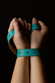 woman's hands restrained with blue leather belt on black background