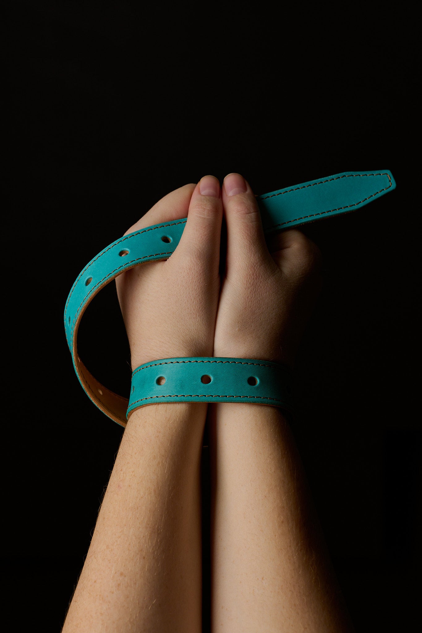 woman's hands restrained with blue leather belt on black background
