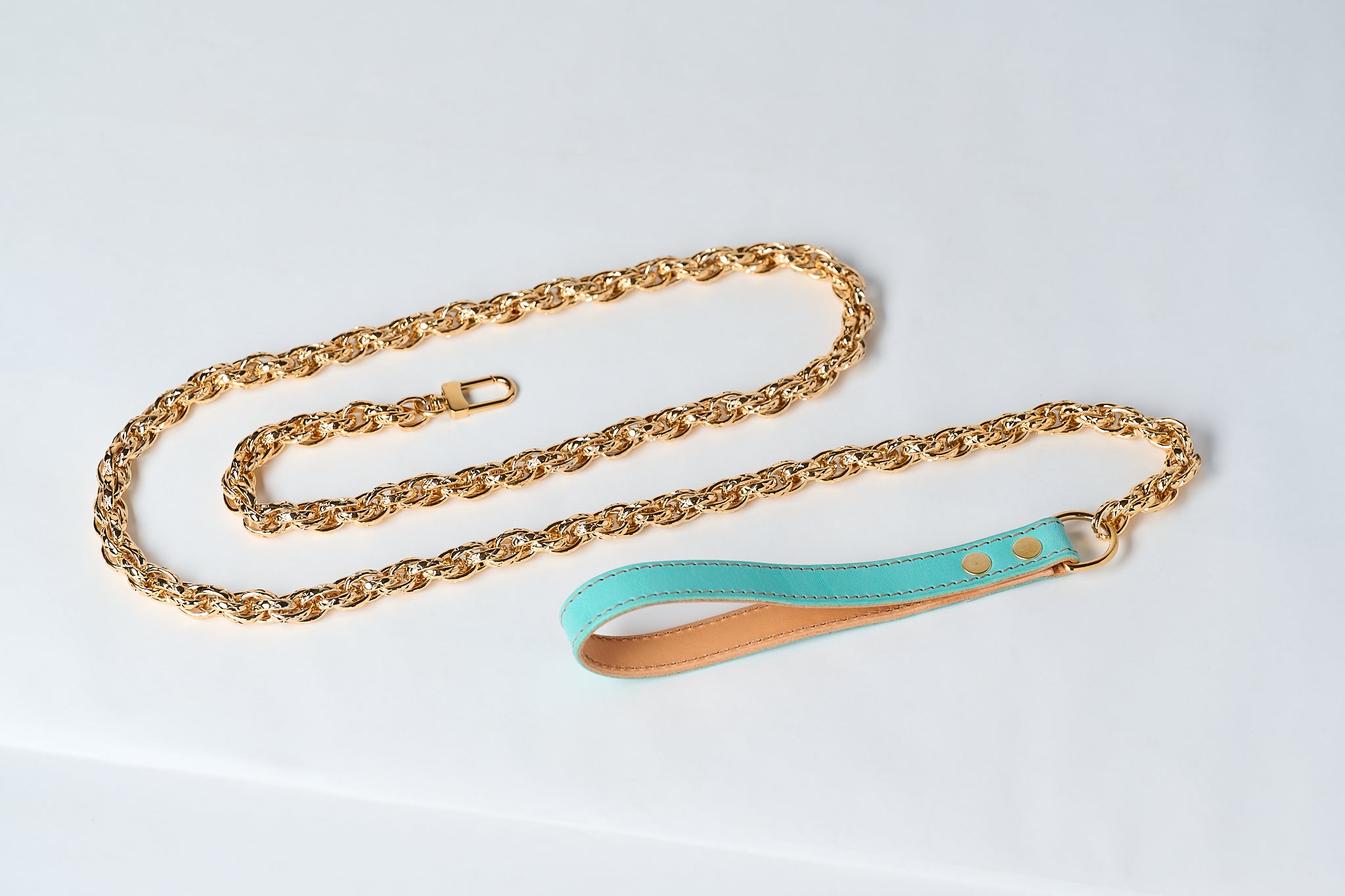 Gold chain with a turquoise leather strap on a light gray background