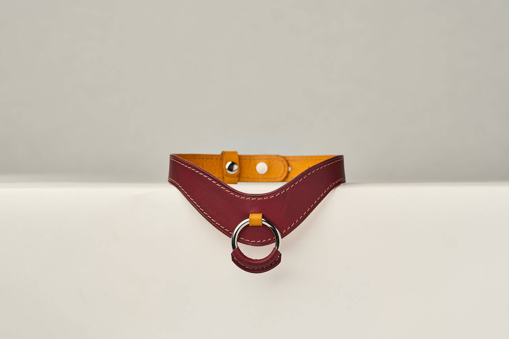 burgundy and yellow leather necklace with a ring on a beige background