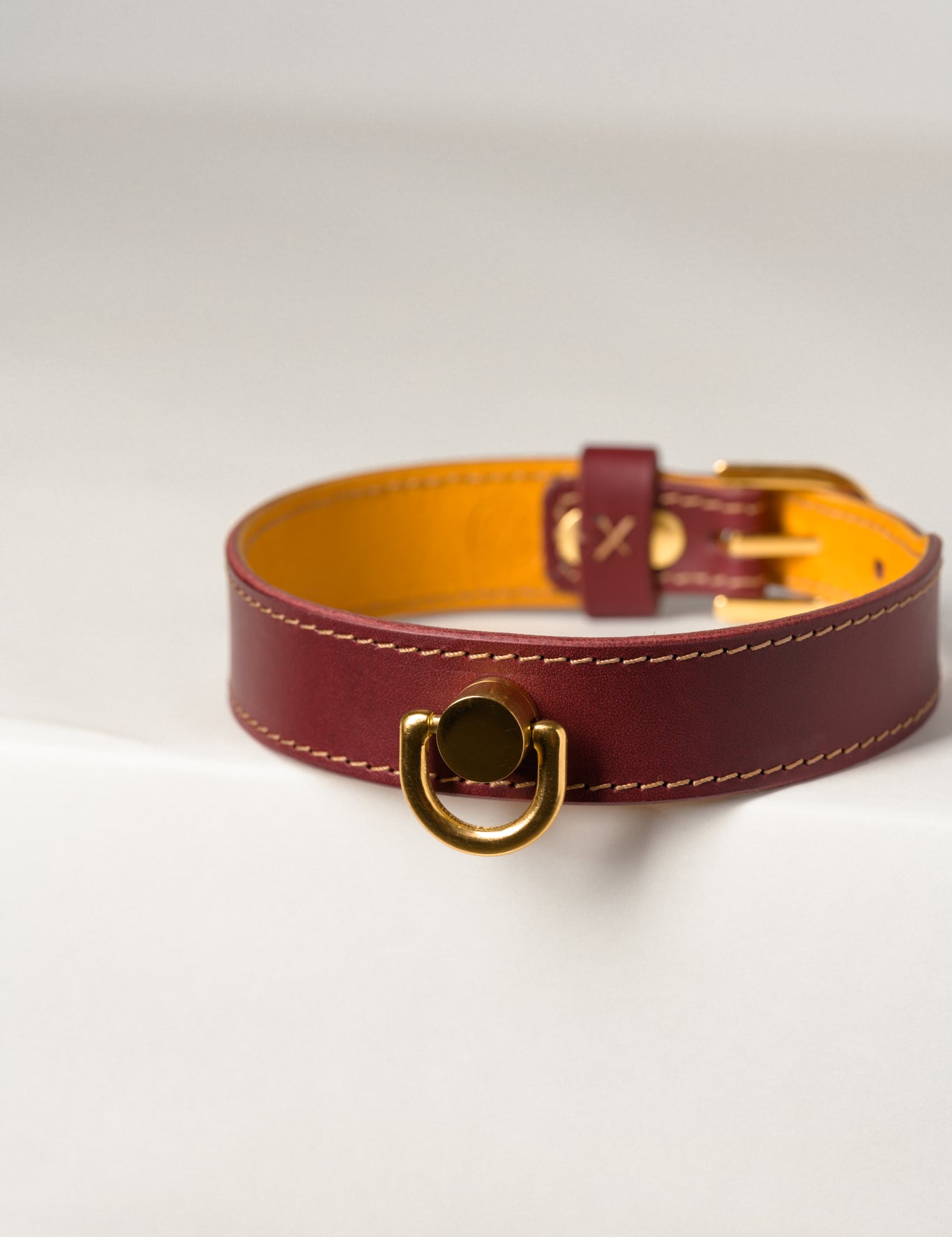 A close-up image of a luxury leather necklace with a gold stainless steel buckle, predominantly burgundy in color.