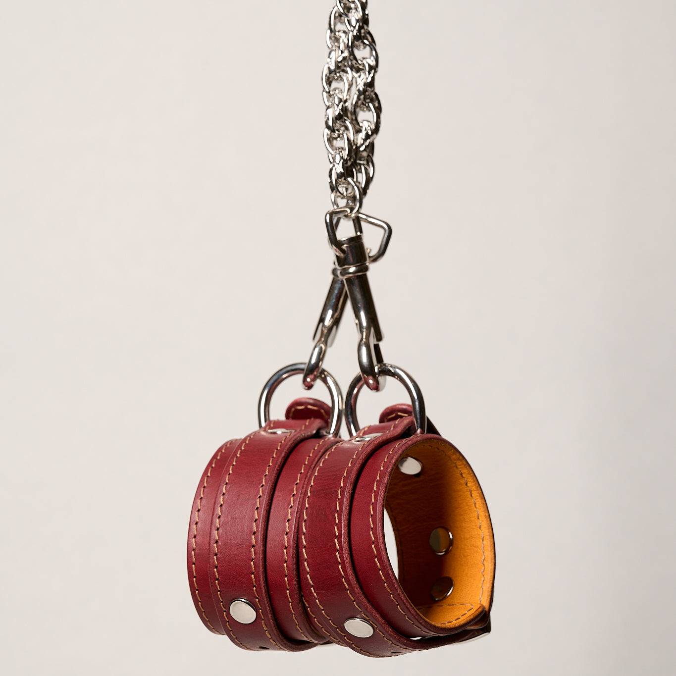 Red leather wrist cuffs with a silver chain on a light gray background