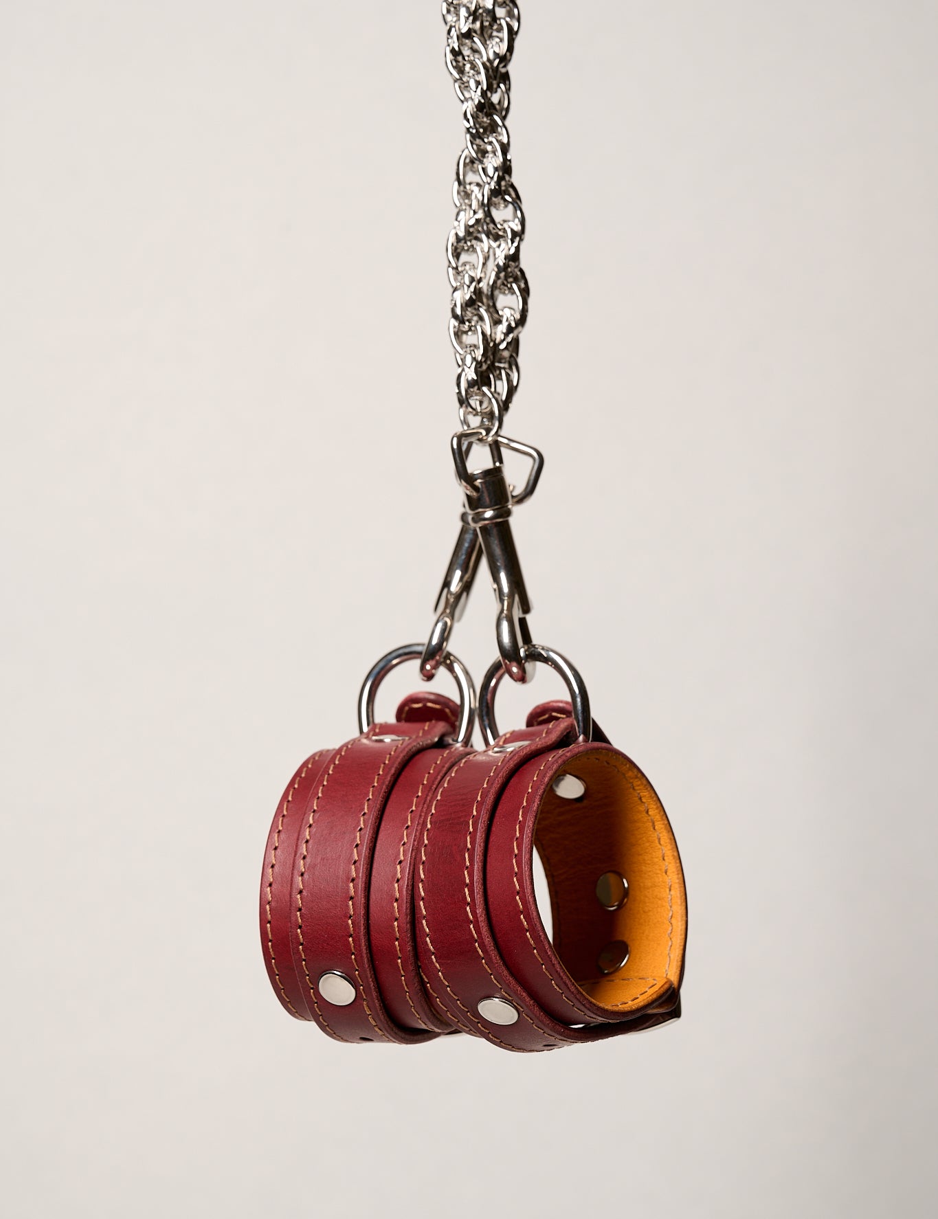 Red leather wrist cuffs with a silver chain on a light gray background