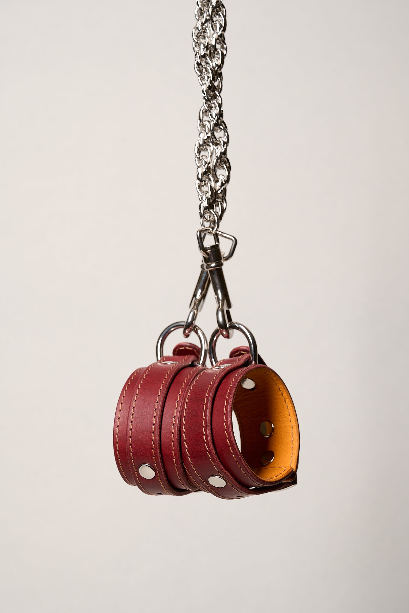 Red leather wrist cuffs with a silver chain on a light gray background