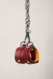 Red leather wrist cuffs with a silver chain on a light gray background