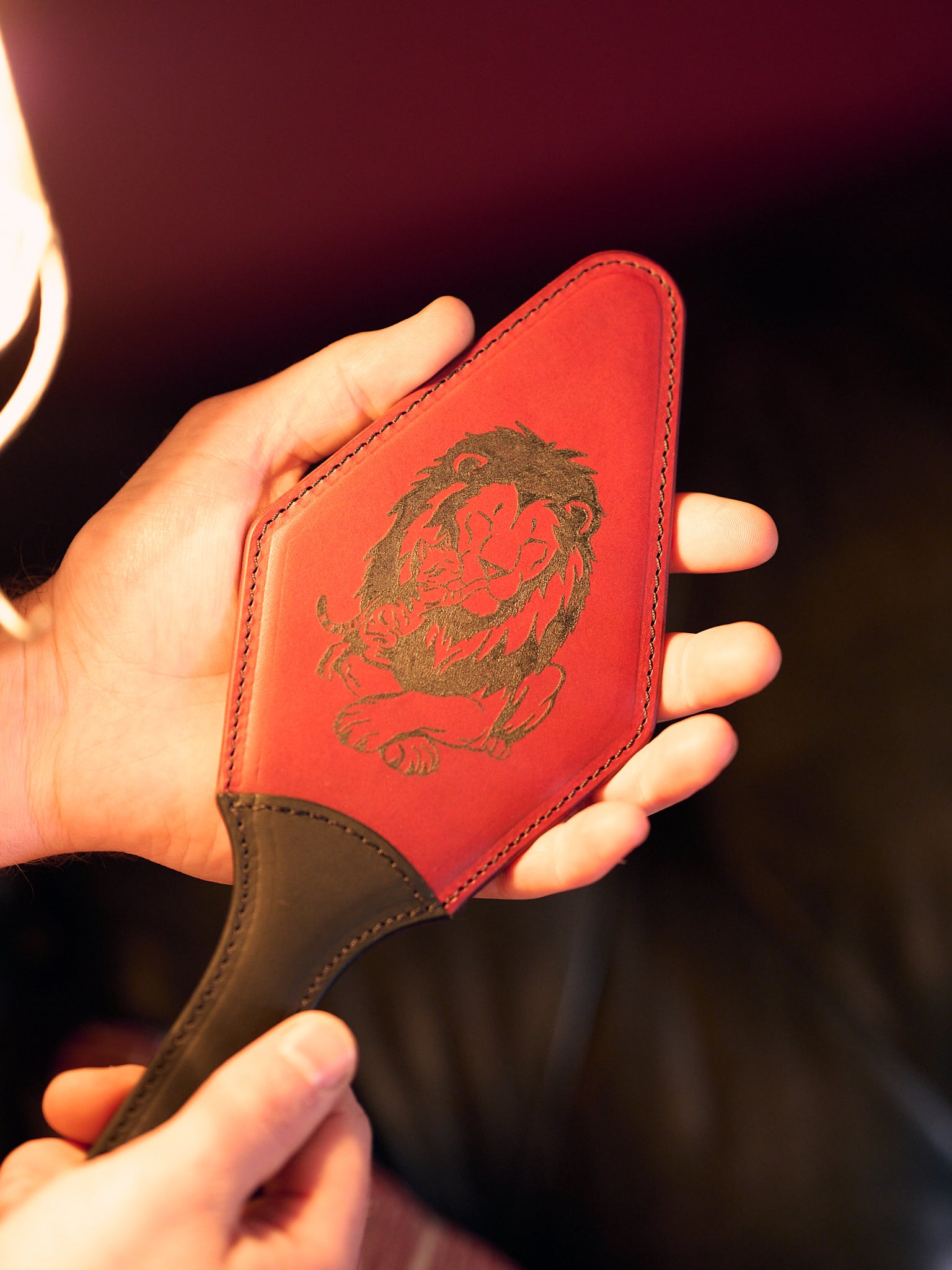 Macro of red leather paddle with a black handle, showing a semi-stiff construction, man holding with tattooed black picture of lion and kitten.