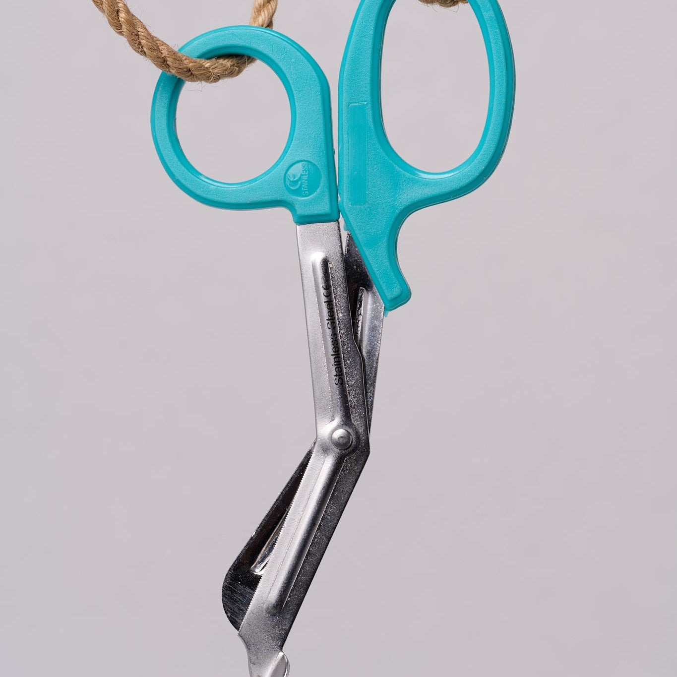 Silver emergency shears with light teal handles hanging from natural jute rope.