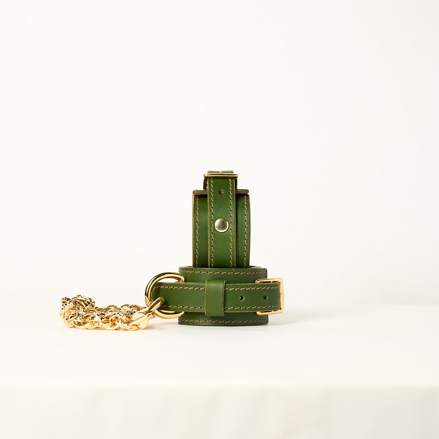 Green leather wrist cuffs with gold chain on a white background