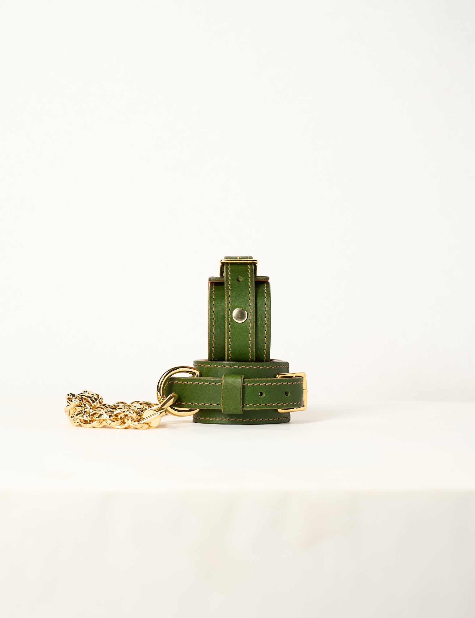 Green leather wrist cuffs with gold chain on a white background