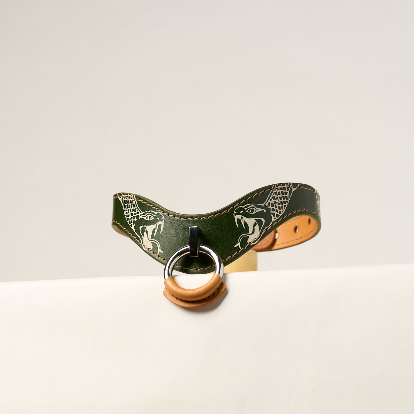 Green leather necklace with a metal ring on a white background tattooed with snakes