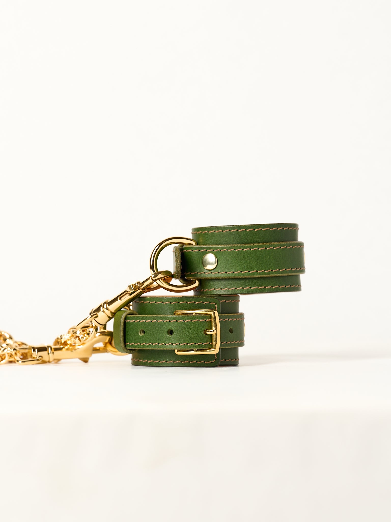 Green leather wirst cuffs  with gold hardware on a white background