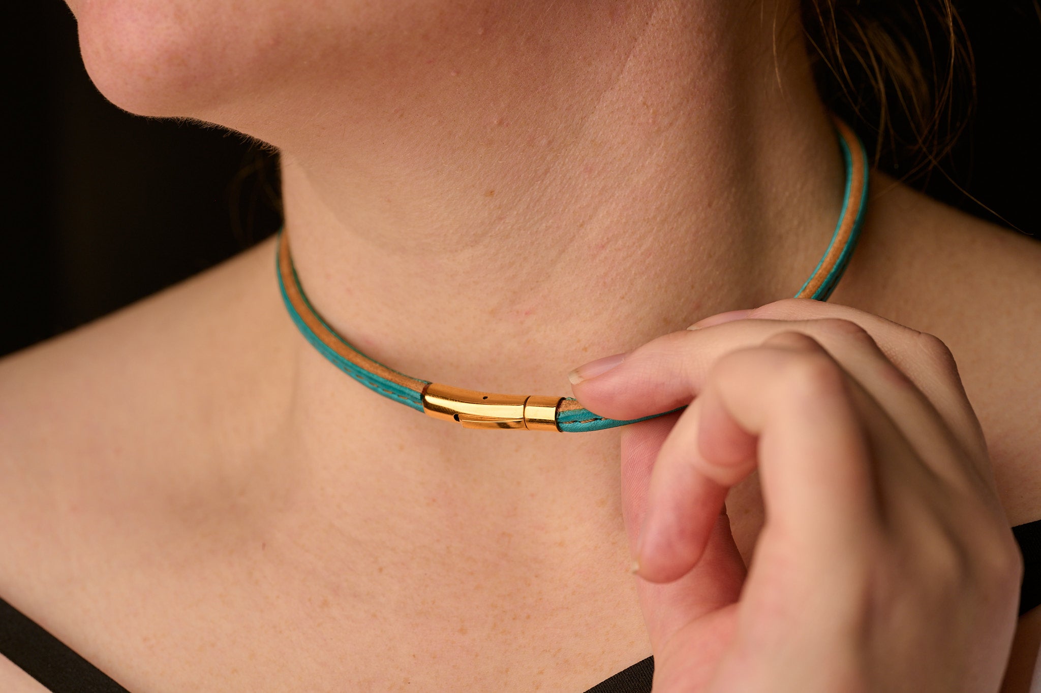 Close-up of a person wearing a turquoise leather necklace with gold clasp.