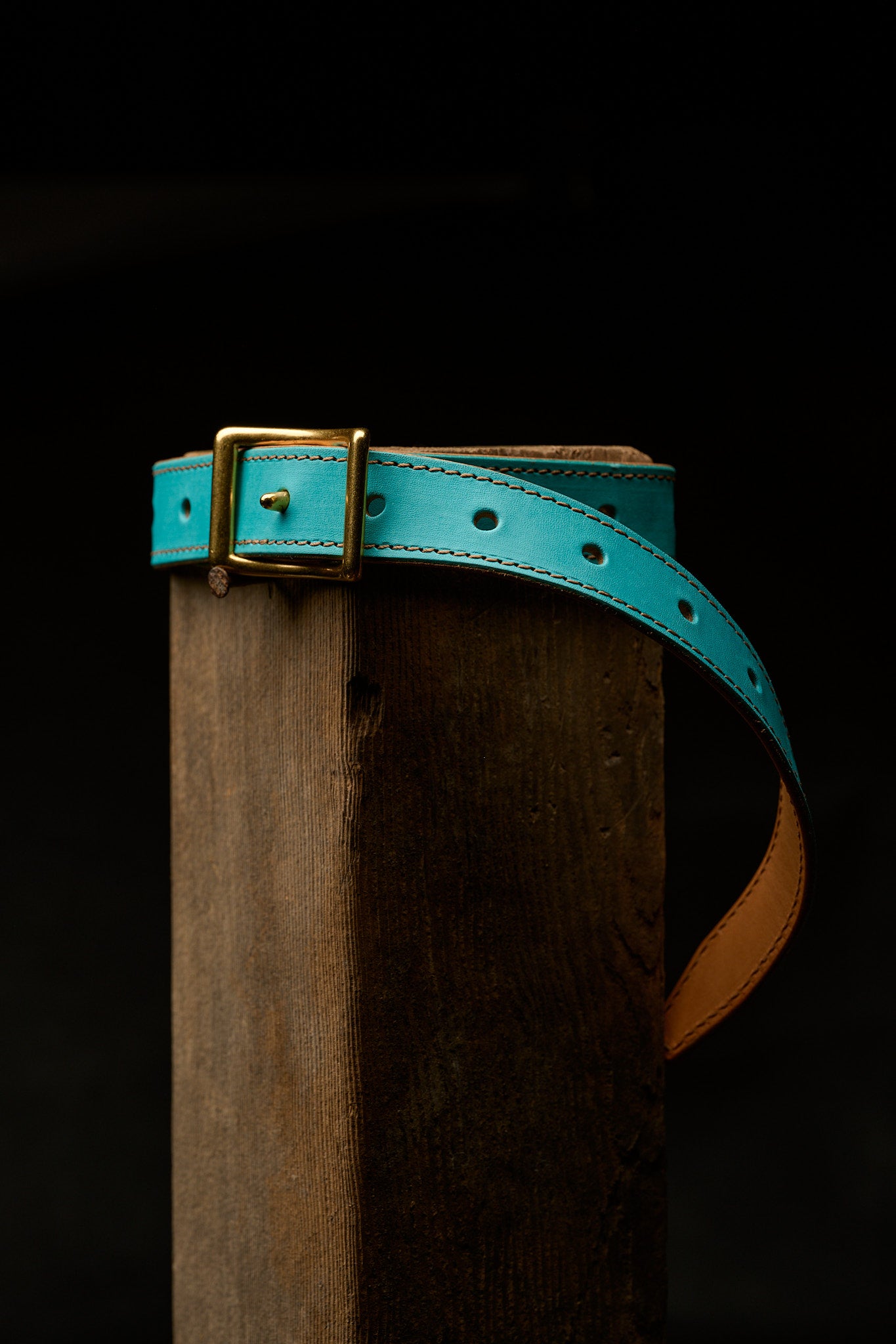 blue leather belt strapped around wood post on black background