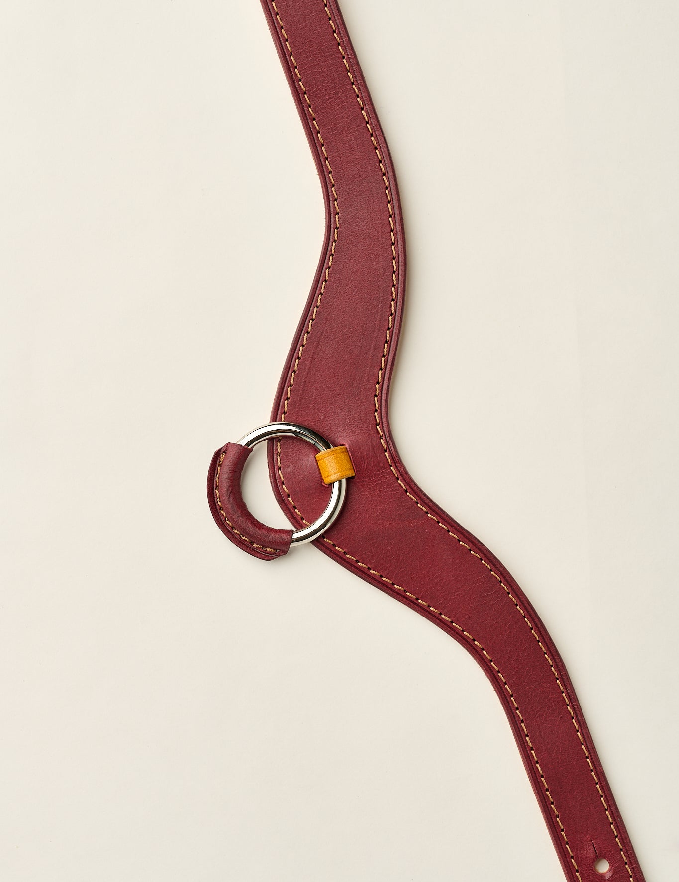 burgundy and yellow leather necklace with a ring on a beige background