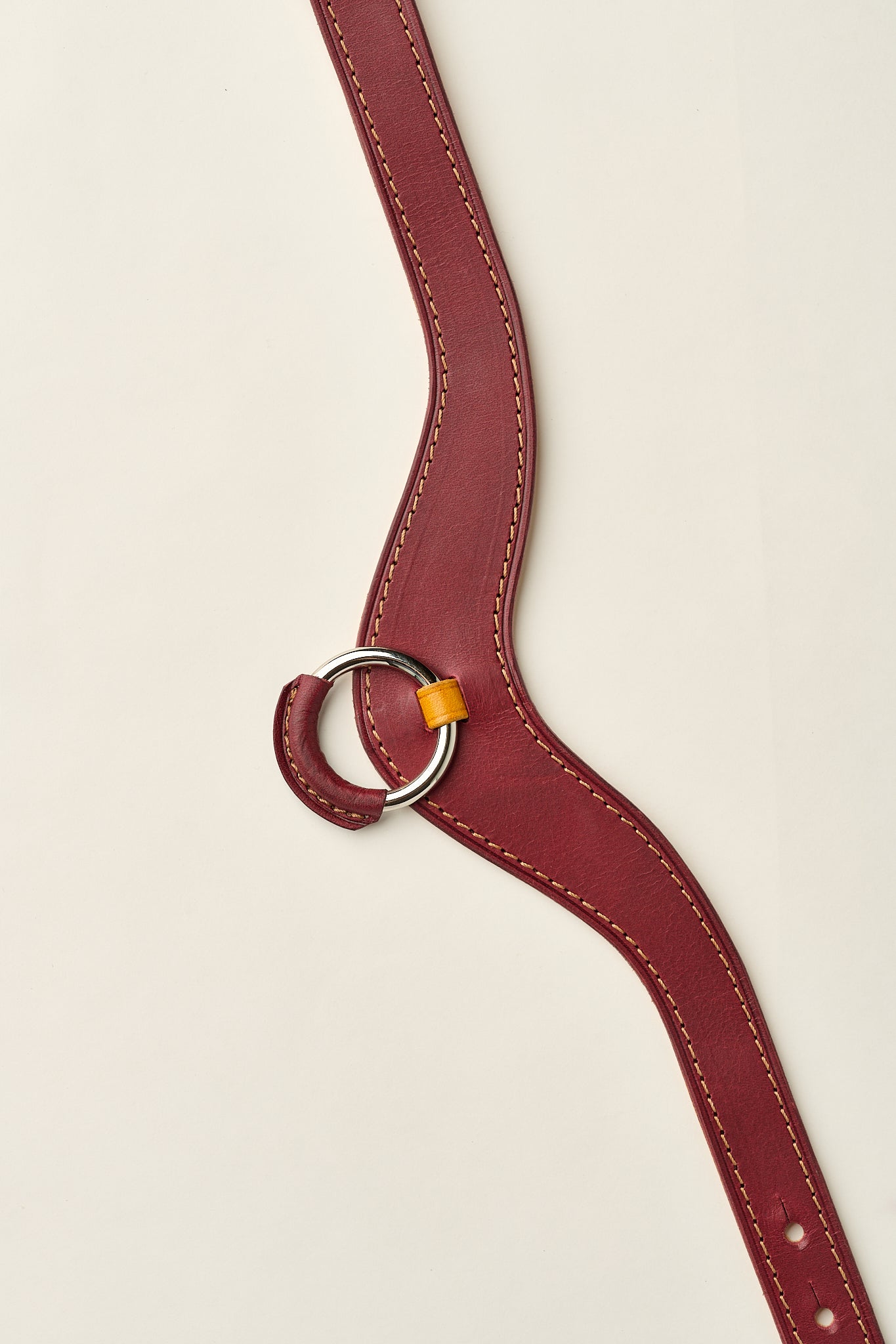 burgundy and yellow leather necklace with a ring on a beige background