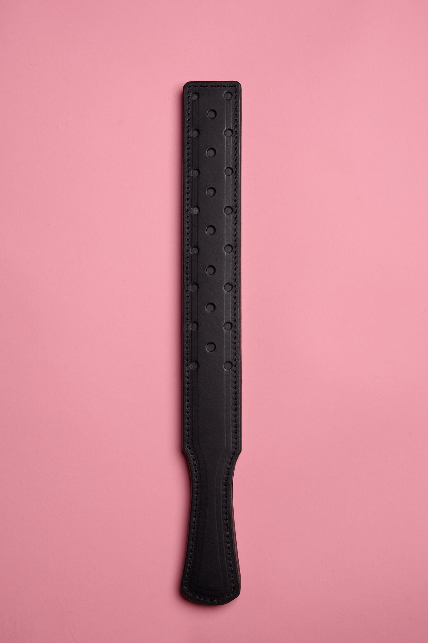 A black leather strap with a fenestrated surface, laid on a pink background.