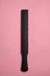 A black leather strap with a fenestrated surface, laid on a pink background.