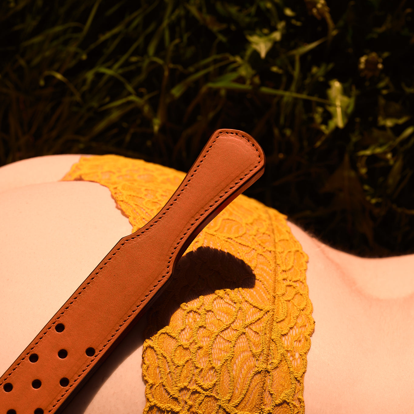 fenestrated leather strap orange brown laying in field of dandelions on a woman in flower bottoms
