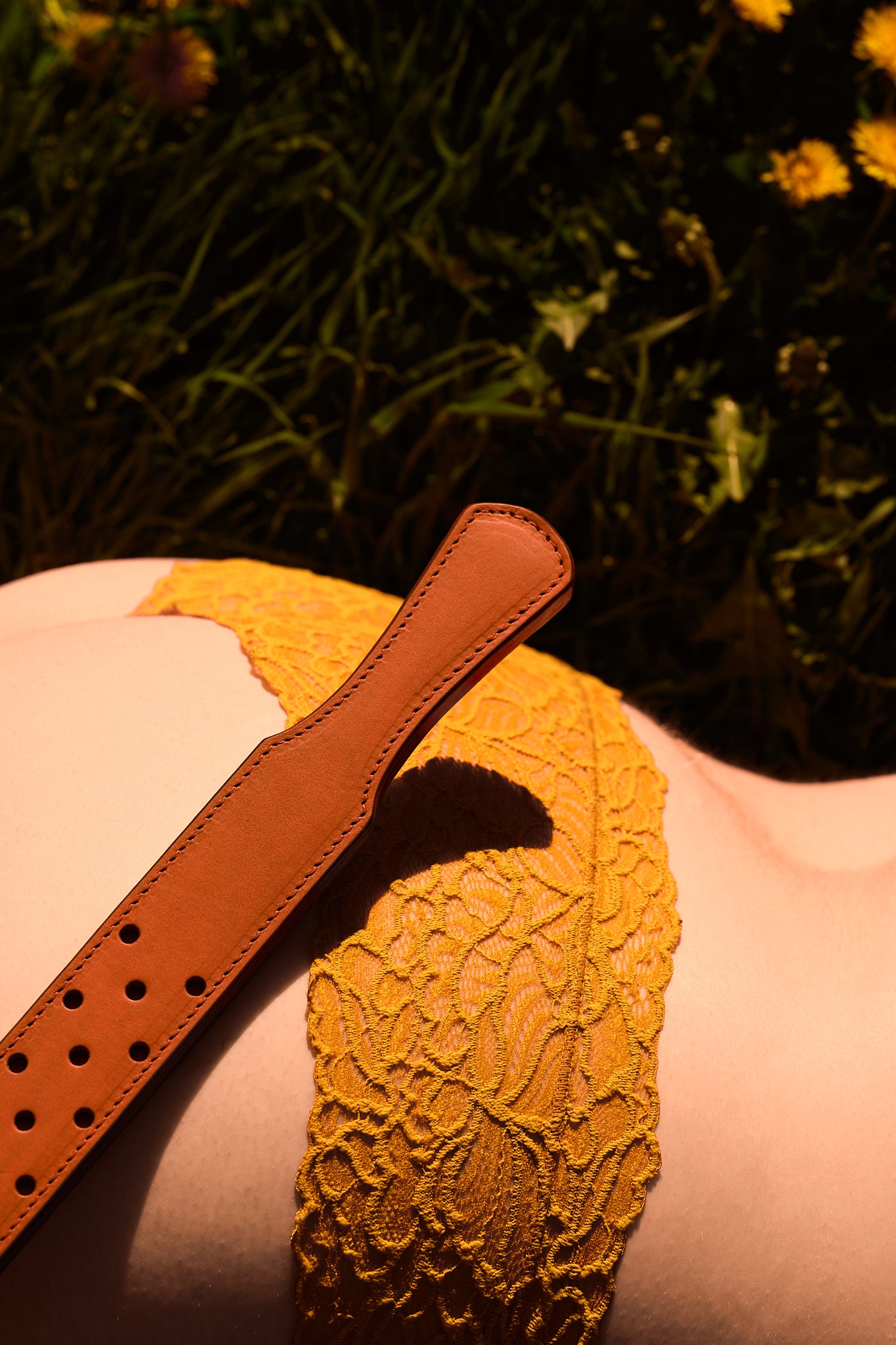 fenestrated leather strap orange brown laying in field of dandelions on a woman in flower bottoms