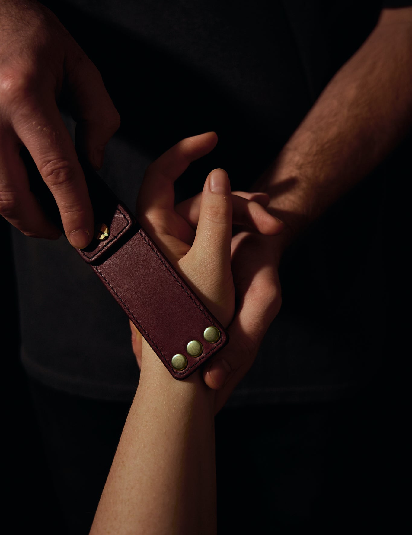 pomegranate leather portable pocket paddle with brass rivets and black thread in a mans hand laying on a womans hand.