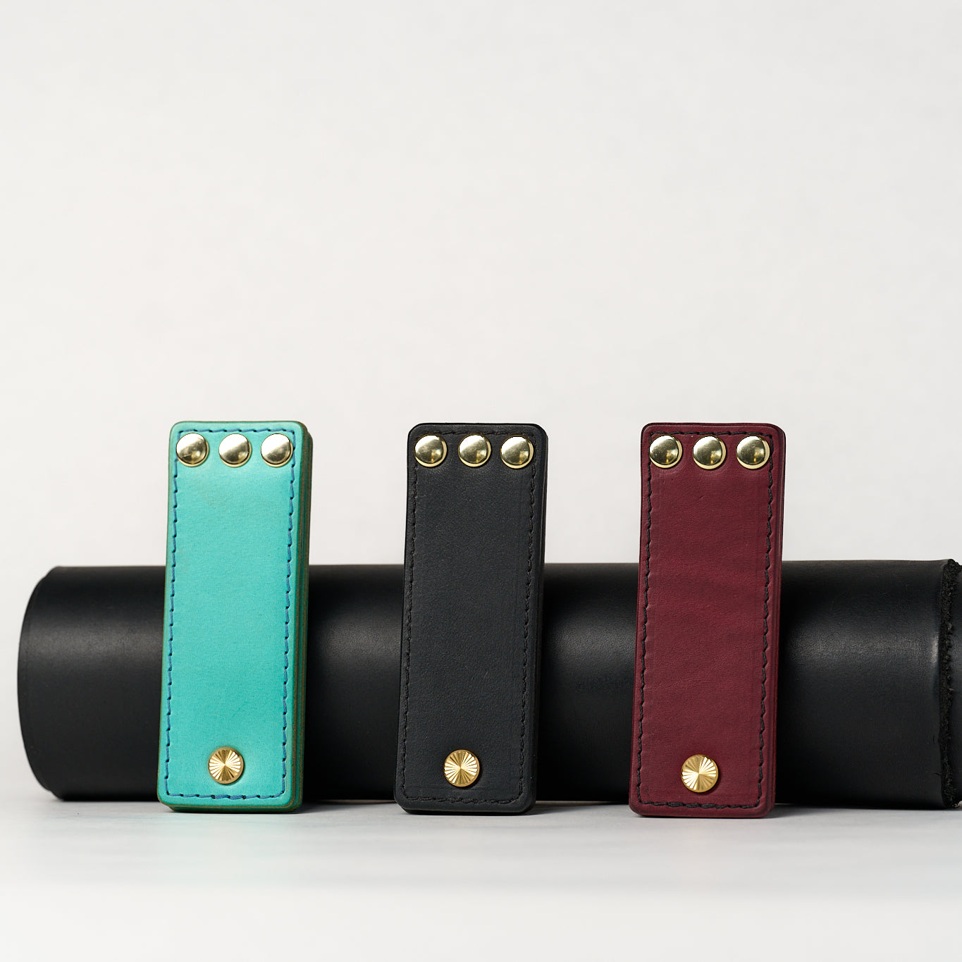 Three leather novelty items in turquoise, black, and red with gold studs on a white background