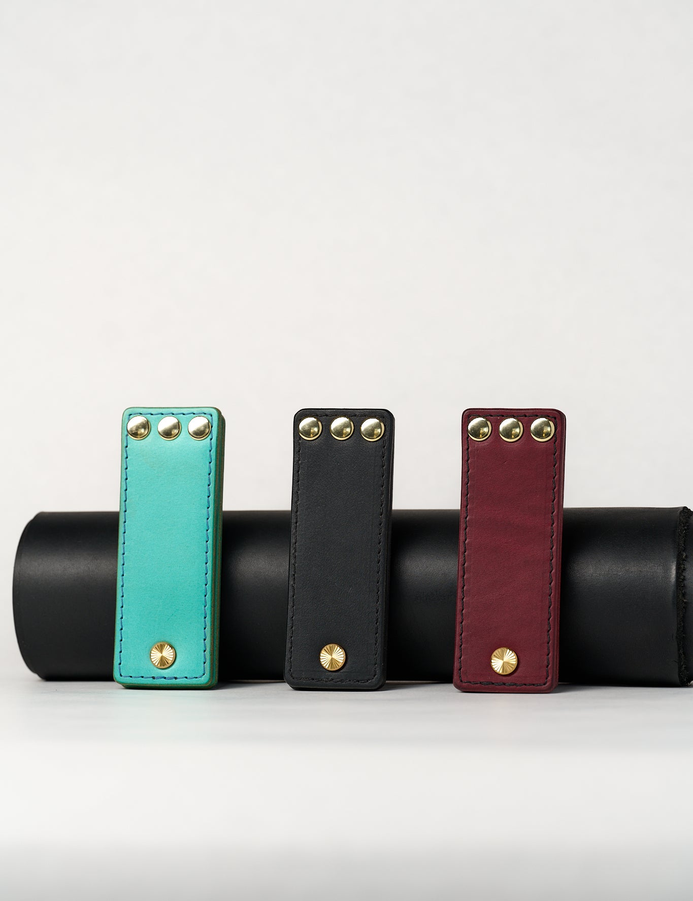 Three leather novelty items in turquoise, black, and red with gold studs on a white background