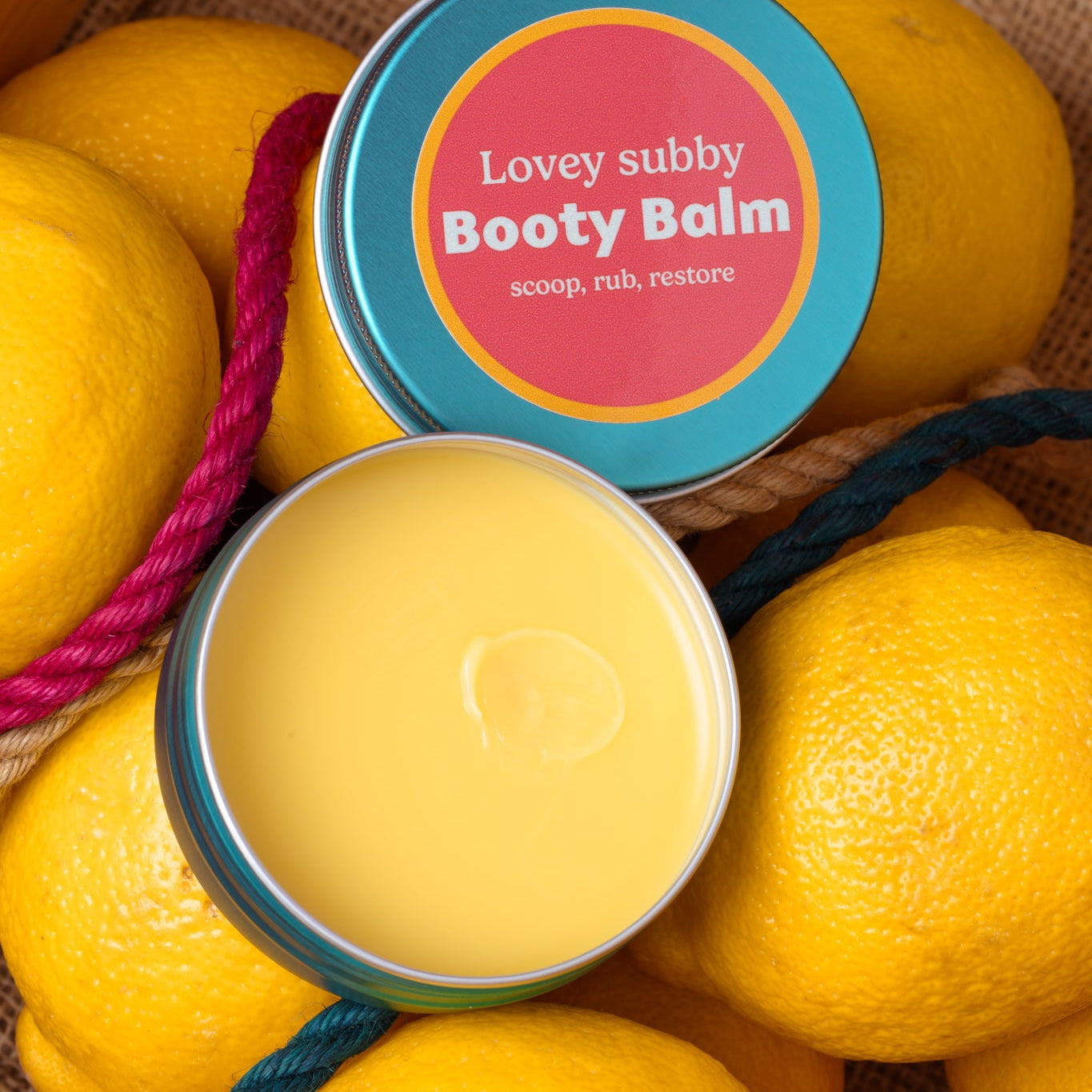 Booty Balm container surrounded by lemons with a colorful label.