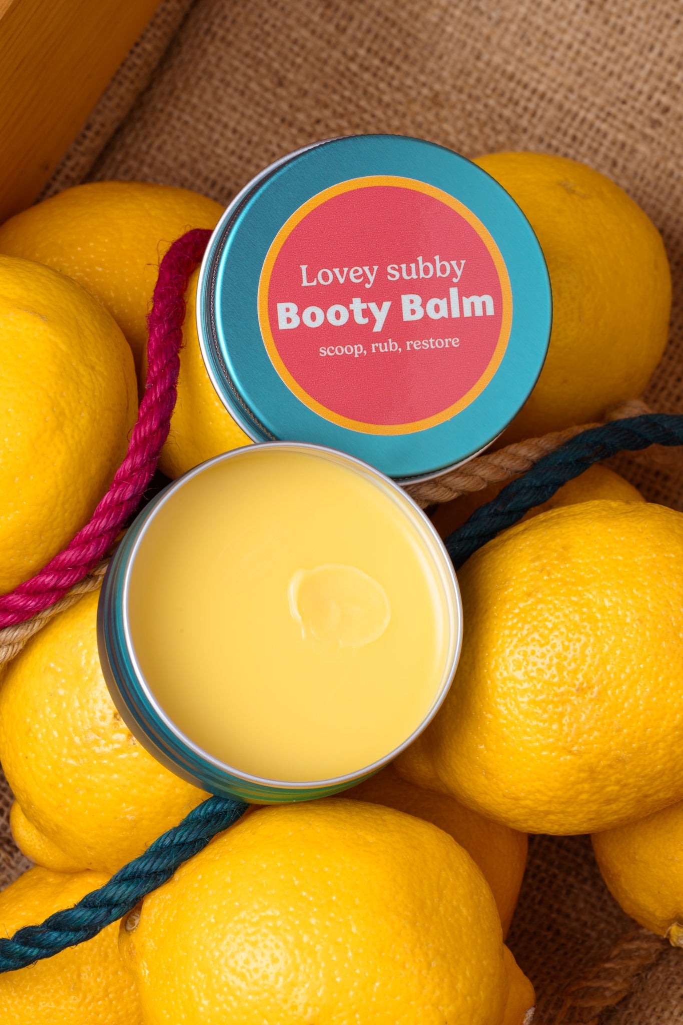 Booty Balm container surrounded by lemons with a colorful label.