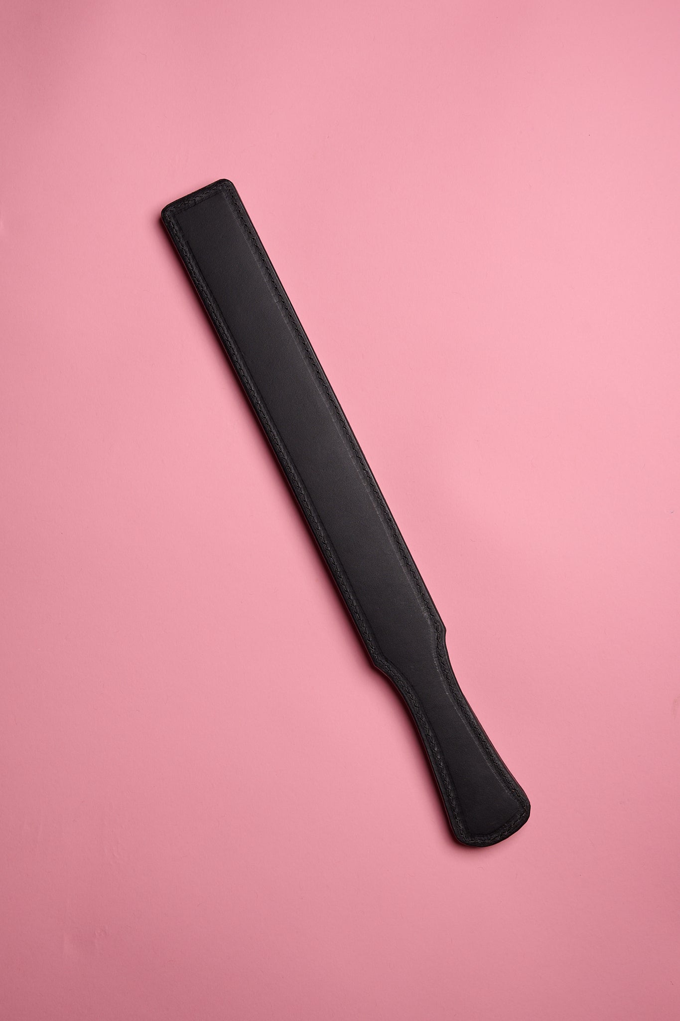 A black leather strap laid on a pink background.