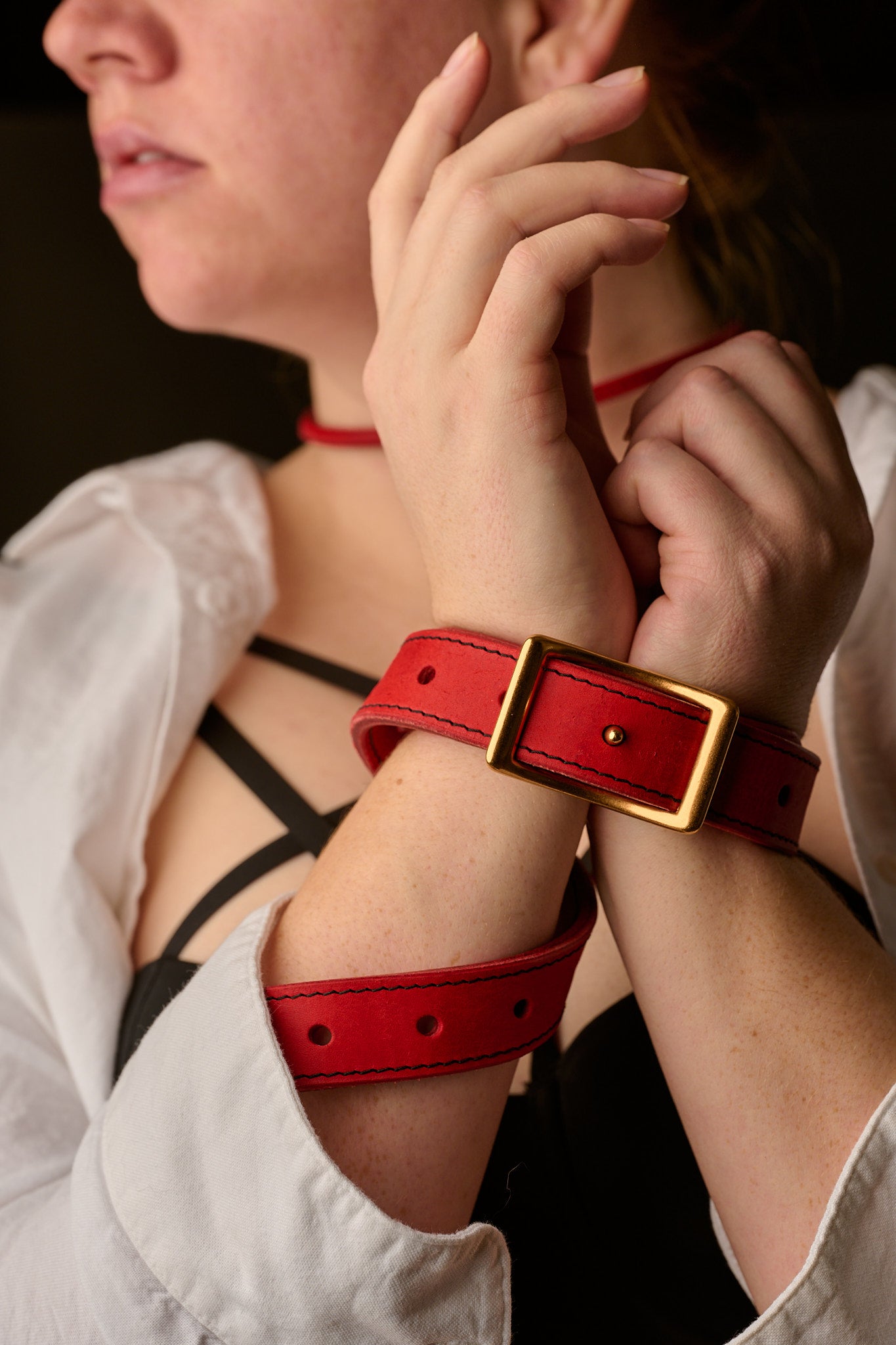 woman's hands restrained with red leather belt on black background