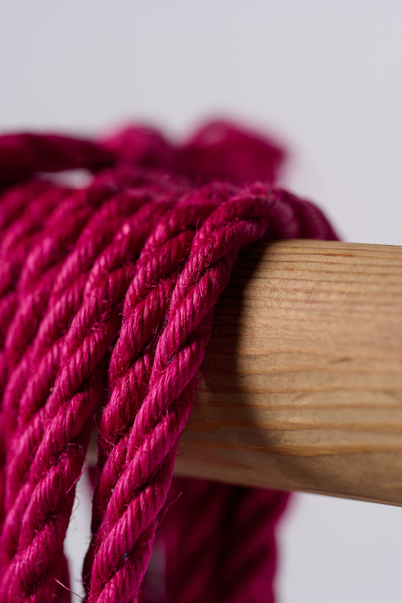 Macro pink jute rope hanging over wooden rod on white background.